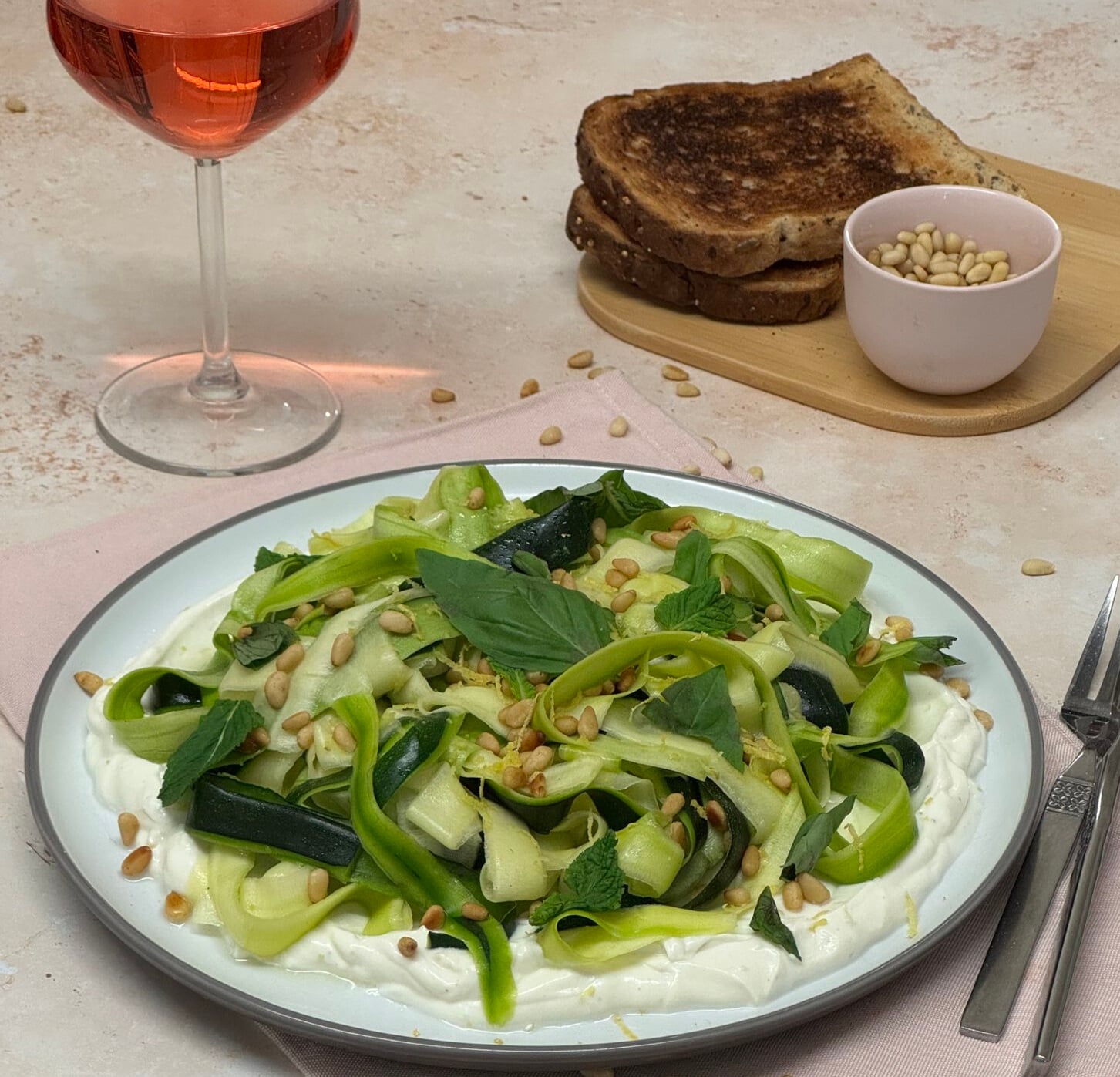 No-cook zucchini ribbon salad with whipped lemon ricotta, basil, mint, toasted pine nuts, and lemon zest served on a white plate.