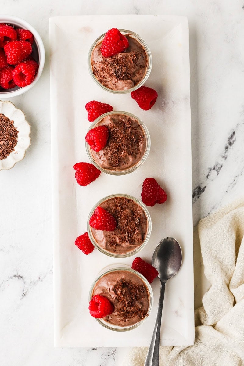 An overhead image of topping the chocolate mousse with raspberries and cocoa nibs.