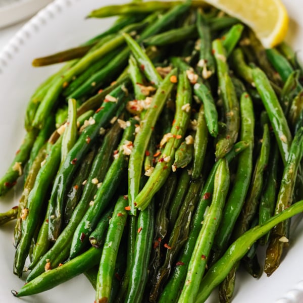 Close-up of skillet green beans with garlic, red pepper flakes, and lemon wedges on a serving platter.