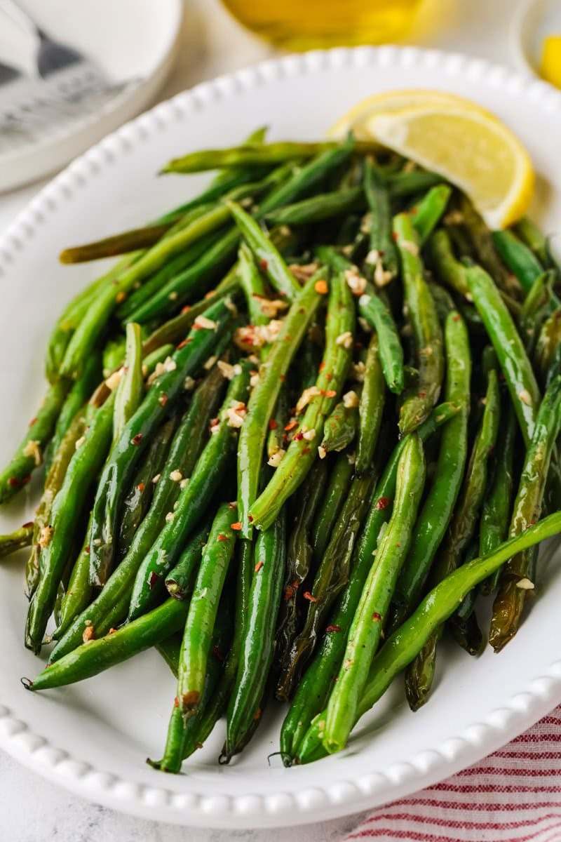 Close-up of skillet green beans with garlic, red pepper flakes, and lemon wedges on a serving platter.