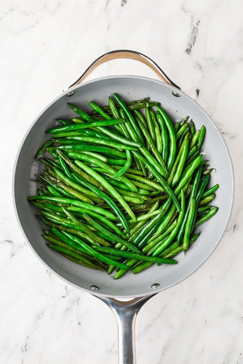 Fresh green beans cooking in a skillet after being tossed in oil and butter.