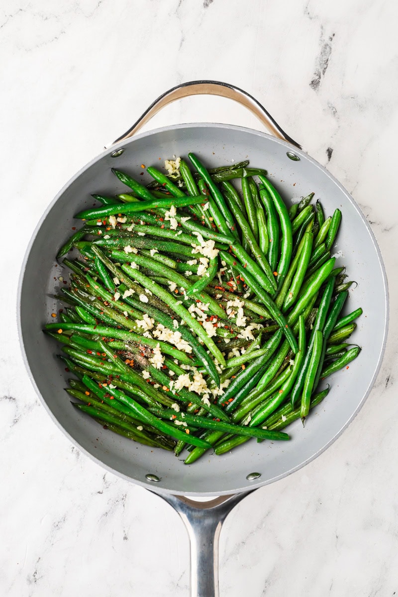 Garlic and seasonings added to green beans in a skillet before the final sauté.