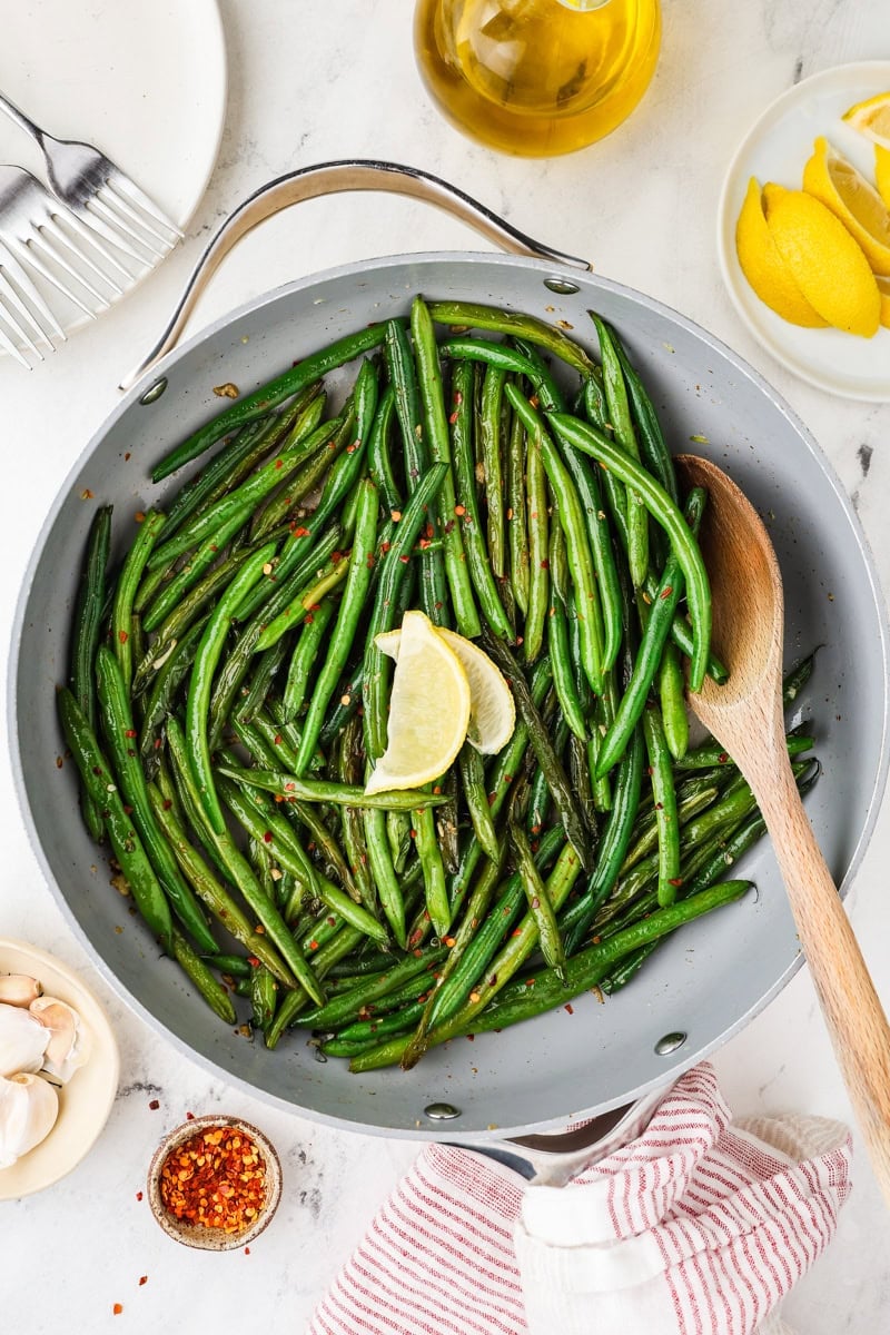 Finished skillet green beans in a pan with lemon wedges ready for serving.