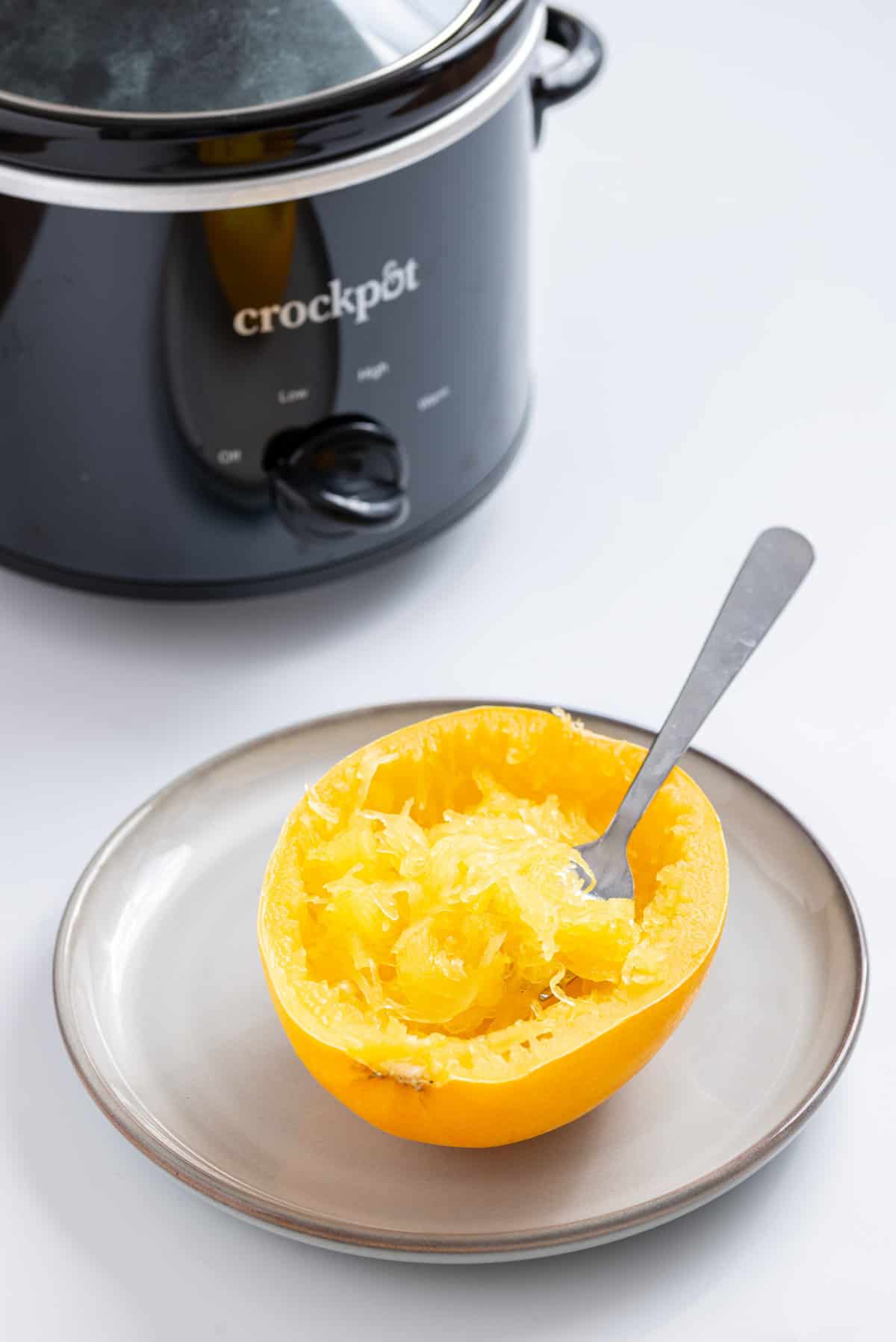 An image of cooked spaghetti squash with strands scraped with a fork and an instant pot behind it.