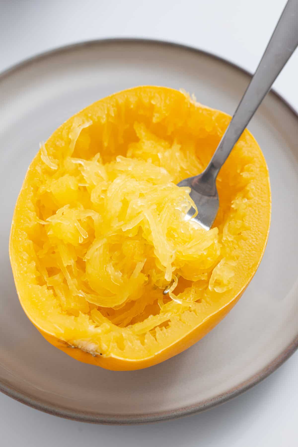 A close up image of cooked spaghetti squash with the strands scraped with a fork.