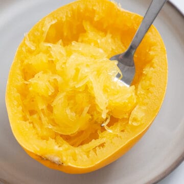 A close up image of cooked spaghetti squash with the strands scraped with a fork.