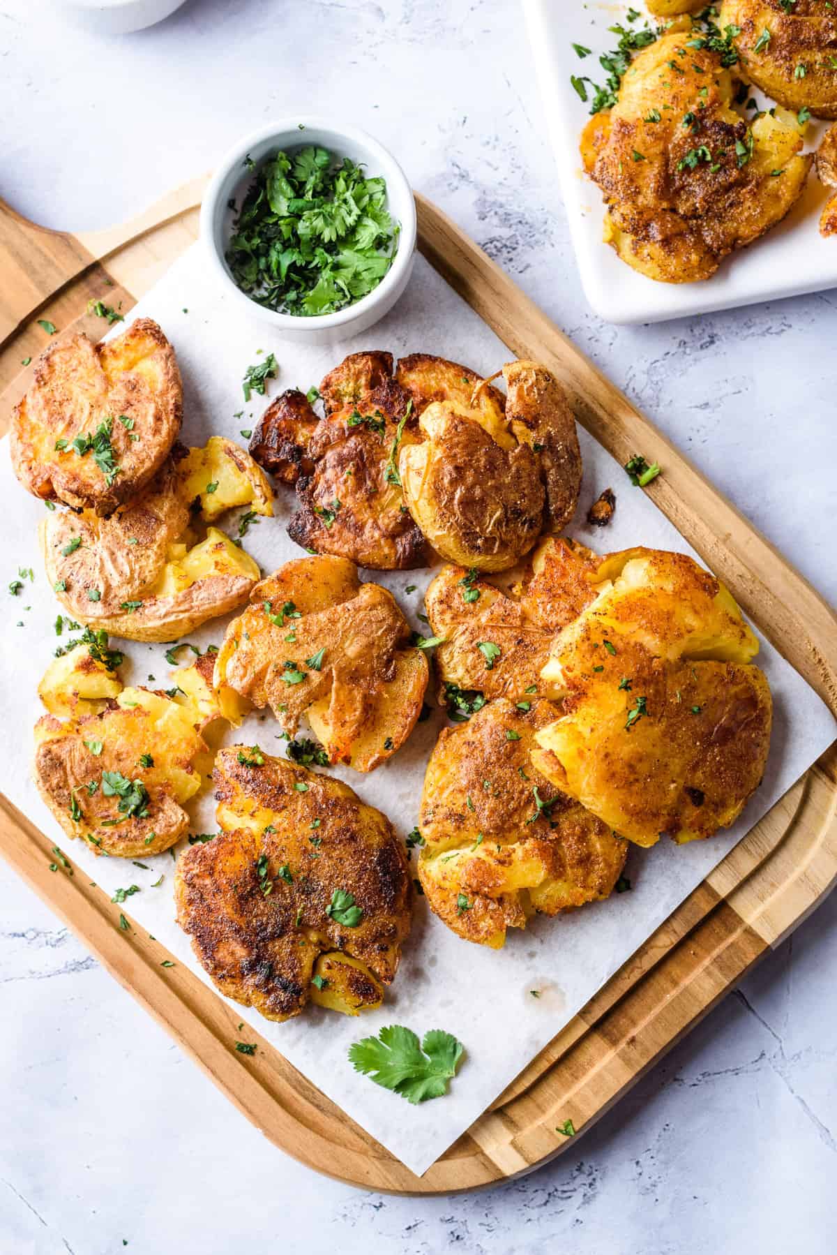 Smashed potatoes on a wooden platter with pinch bowl with parsley. 