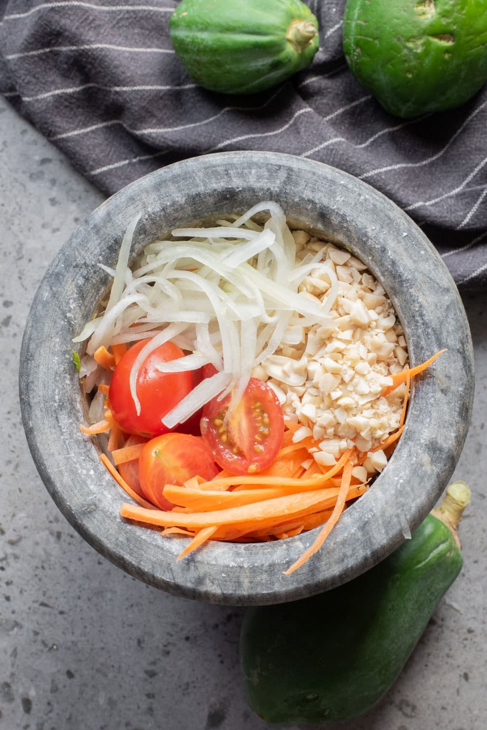 Shredded papaya, carrot, tomatoes, and peanuts added to the mortar.
