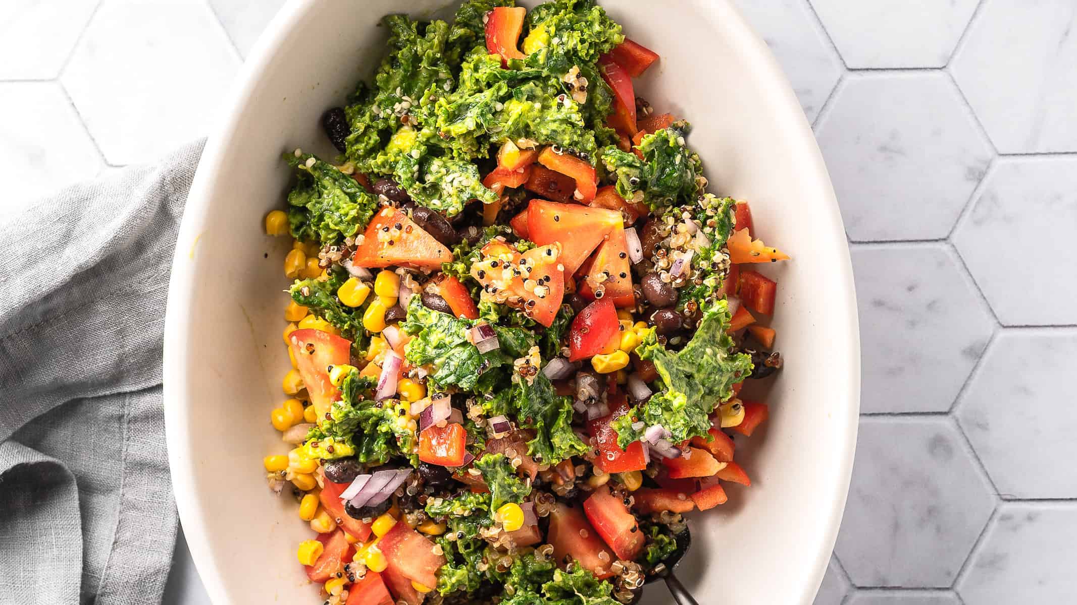 Overhead view of a Southwest kale quinoa bowl on a white oval plate.