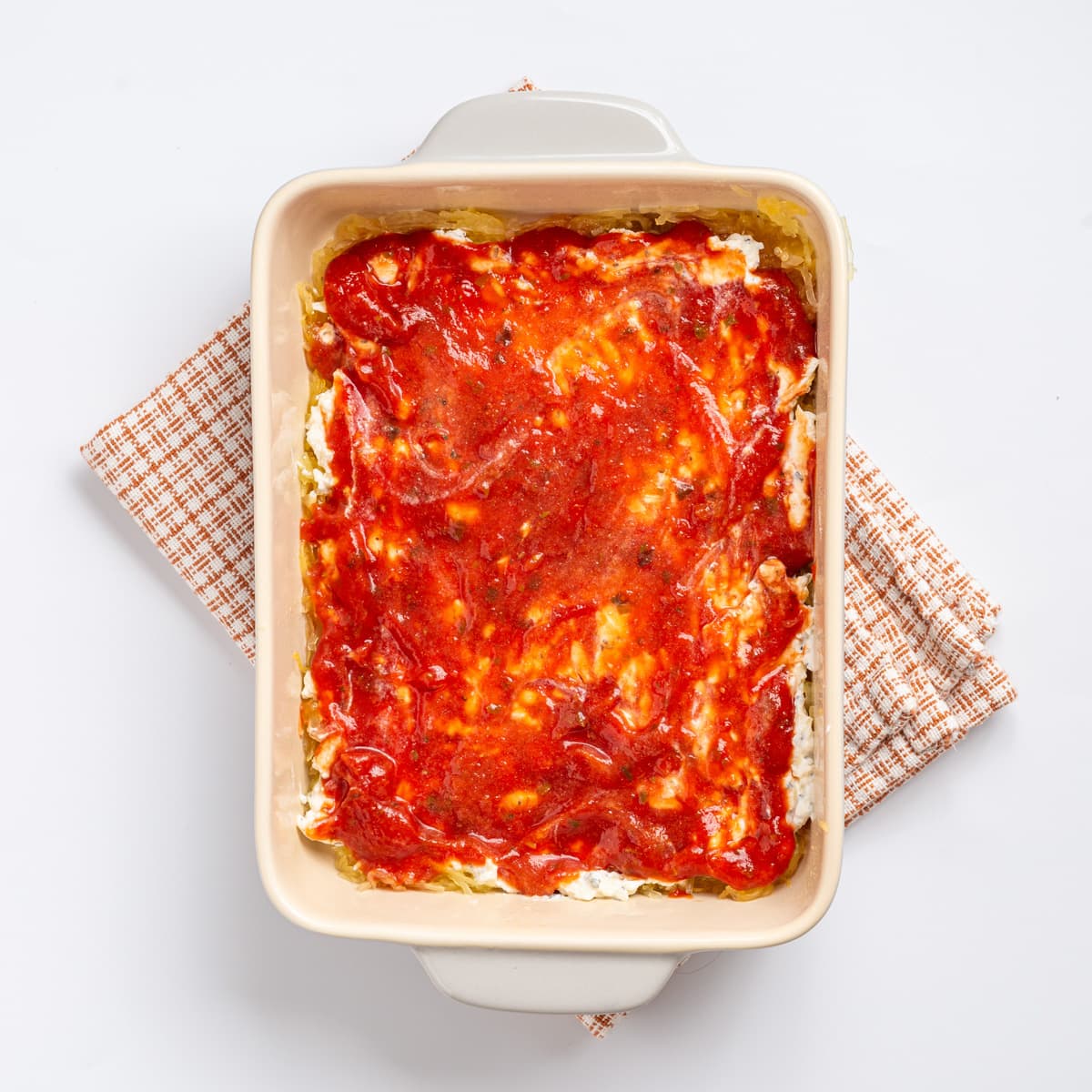 An image of a layer of marinara sauce spread on the baking sheet.