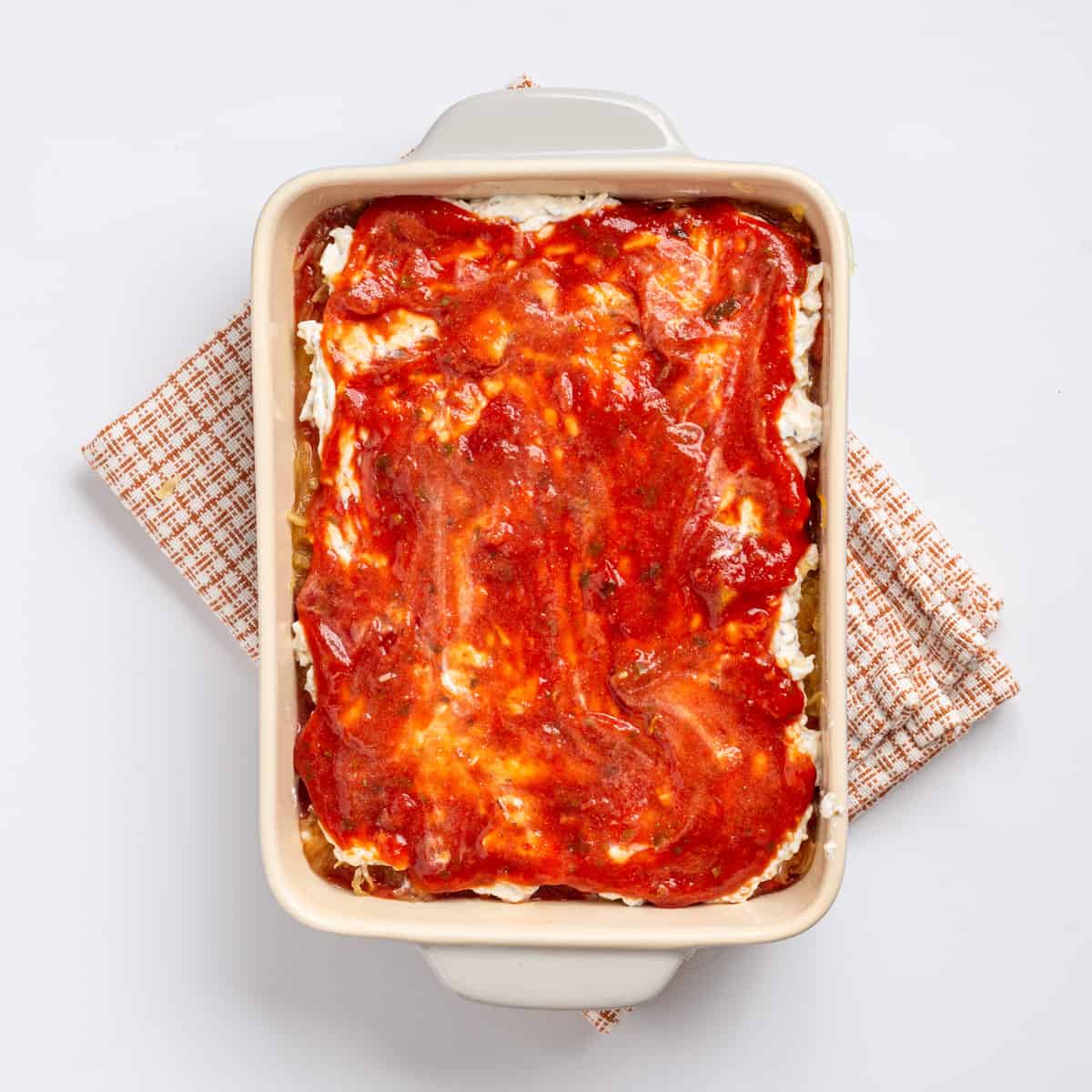An image of another layer of marinara sauce spread on top of the layer of ricotta cheese.