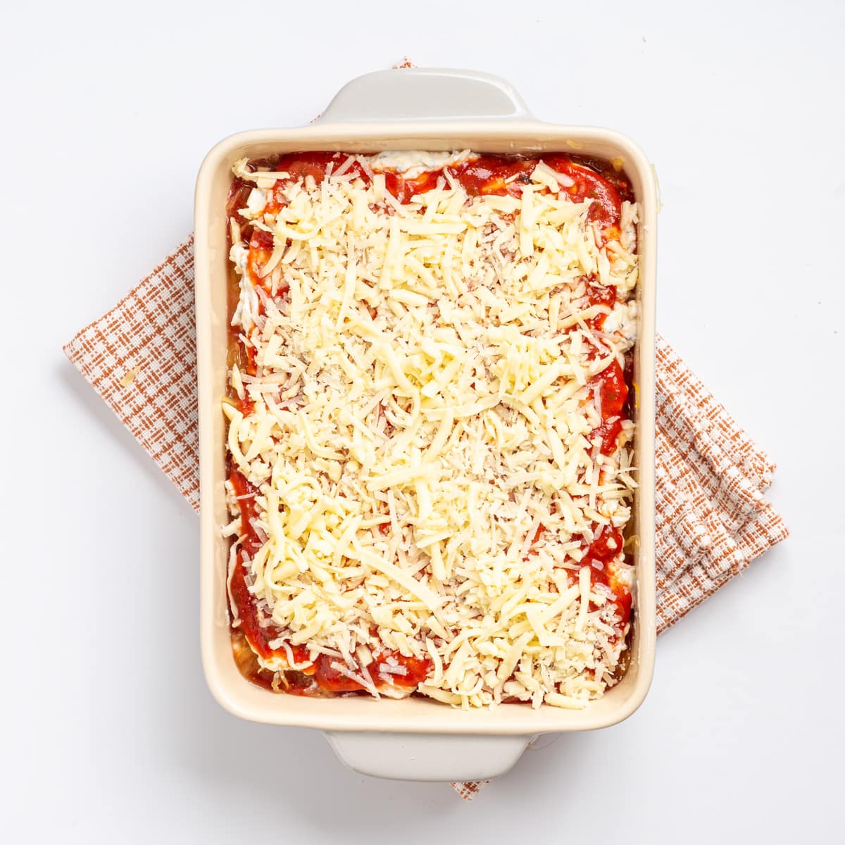 An overhead image of mozzarella and Parmesan cheese sprinkled evenly as a top layer of the lasagna.
