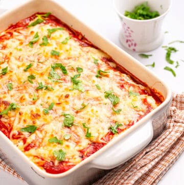 An image of spaghetti squash lasagna in a white baking dish with fresh parsley on the side.