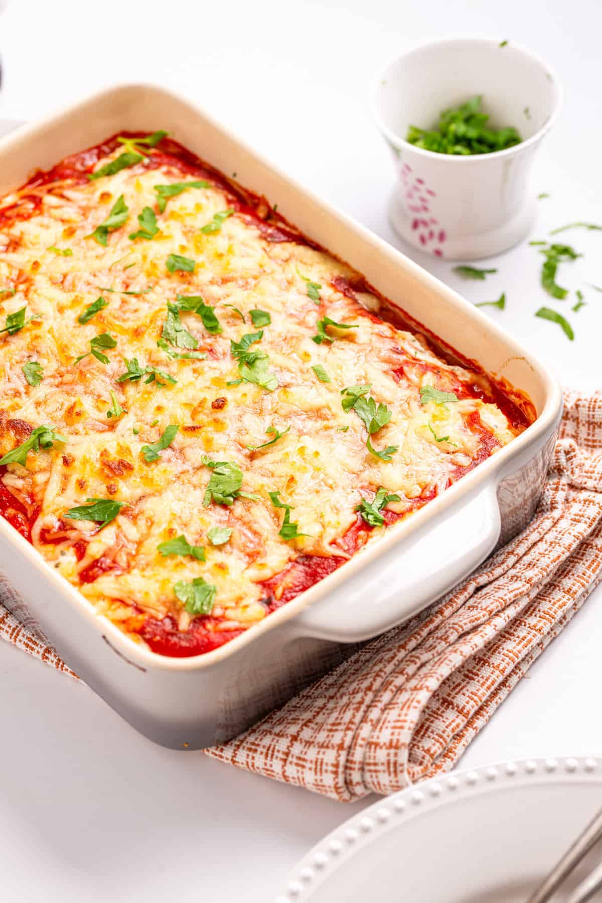 An image of spaghetti squash lasagna in a white baking dish with parsley on the side.