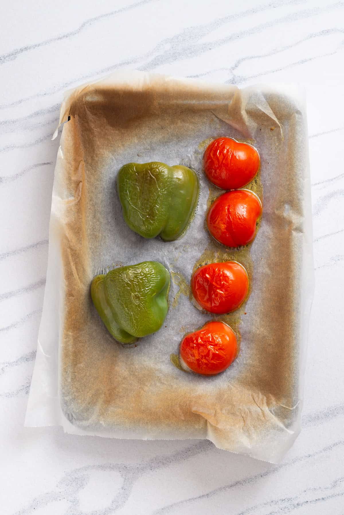 An image of a roasted bell pepper and tomatoes, in a baking pan.