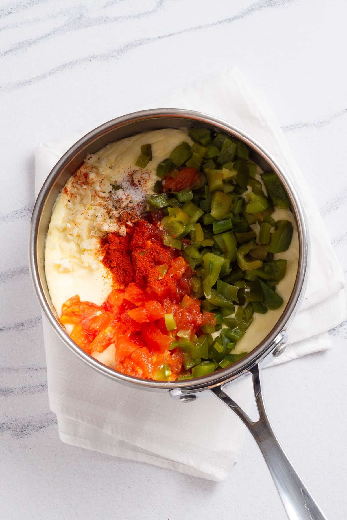 An image of 3-cheese dip combined with spices and roasted veggies in a saucepan.
