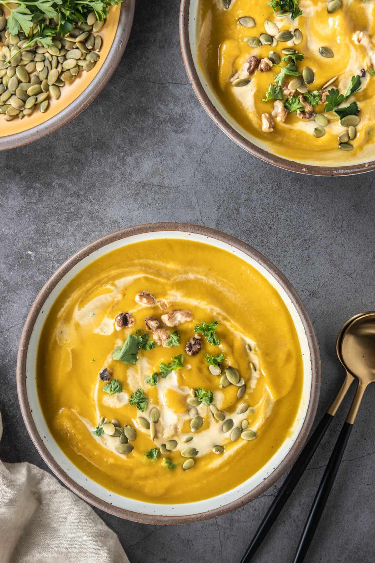 Two bowls of pumpkin soup with garnishes in the background