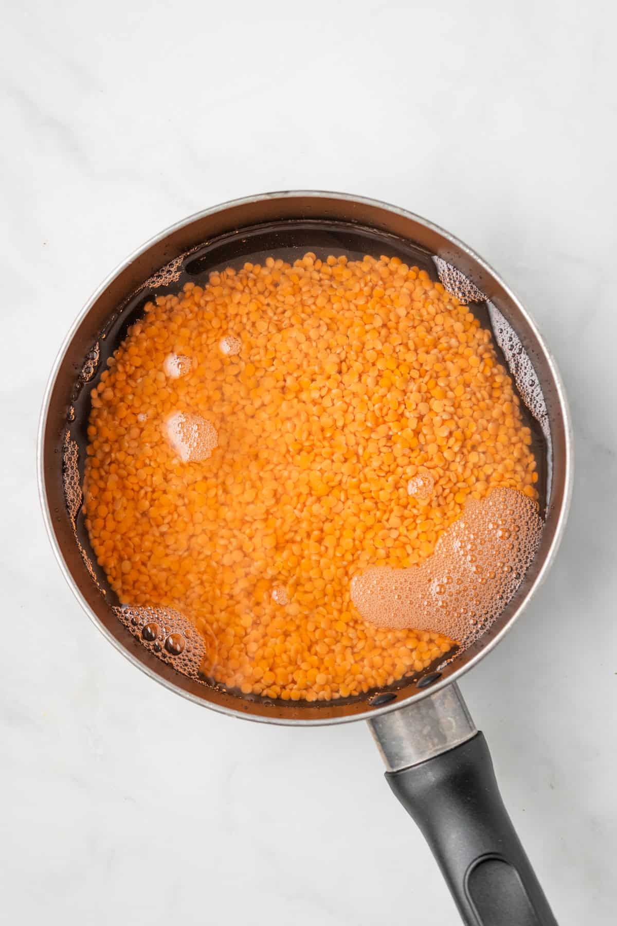 An overhead image of combining water and red lentils to soften.