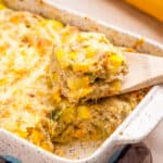 A close up shot of Squash Casserole with Stuffing served on a baking dish with a wooden spoon