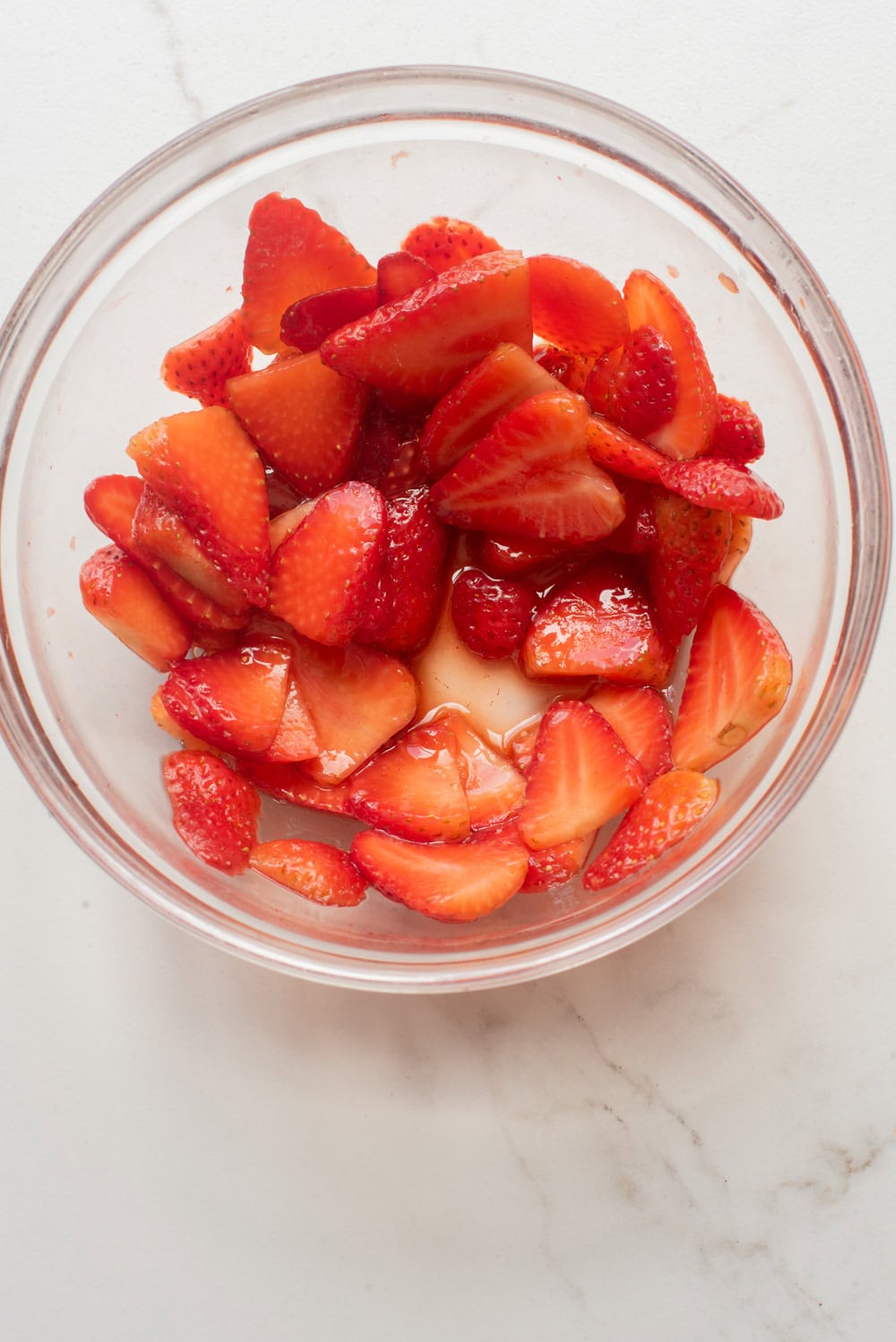 Sliced strawberries macerating with balsamic vinegar and sugar in a bowl.