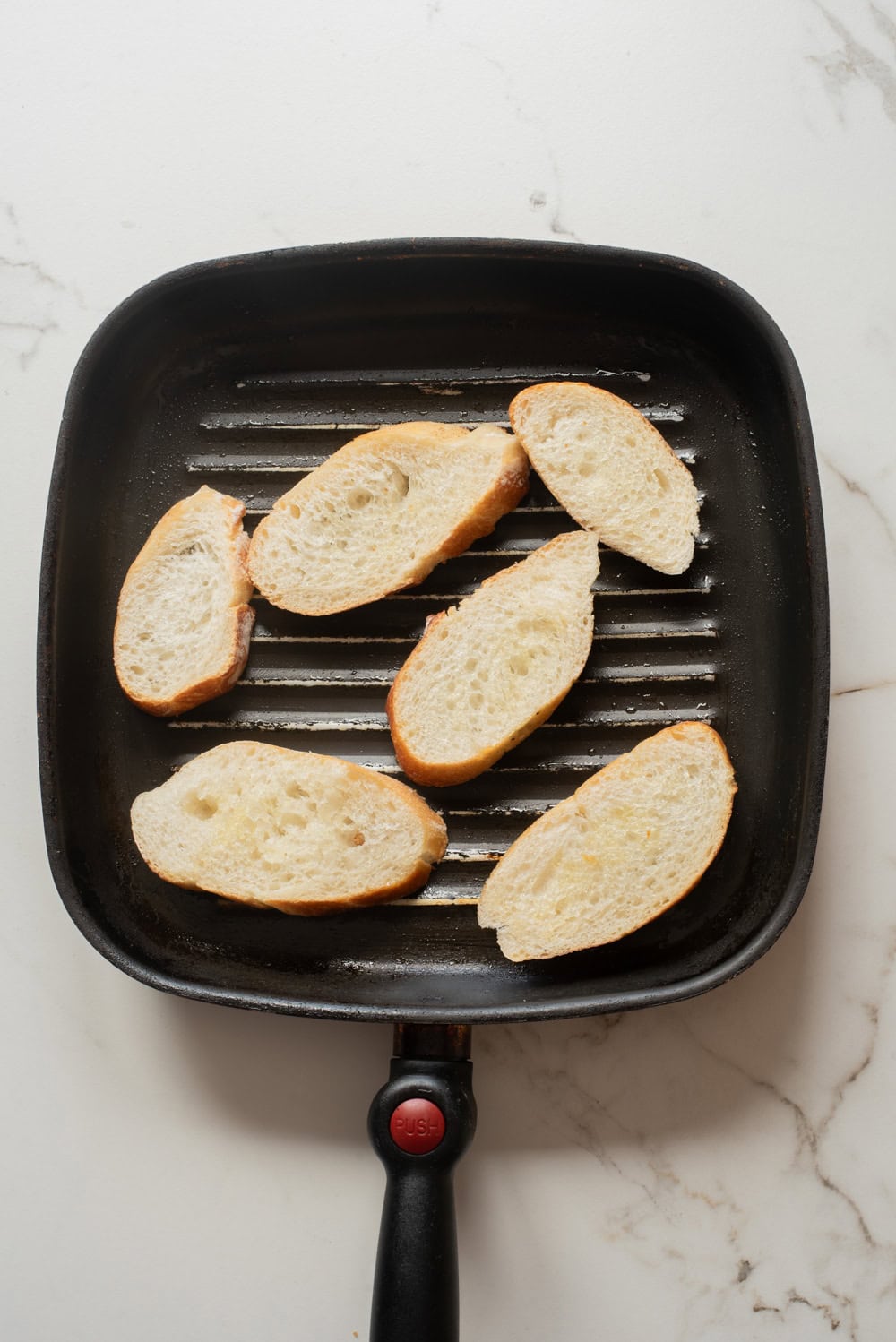 Baguette slices toasting in a grill pan until crisp and lightly charred.