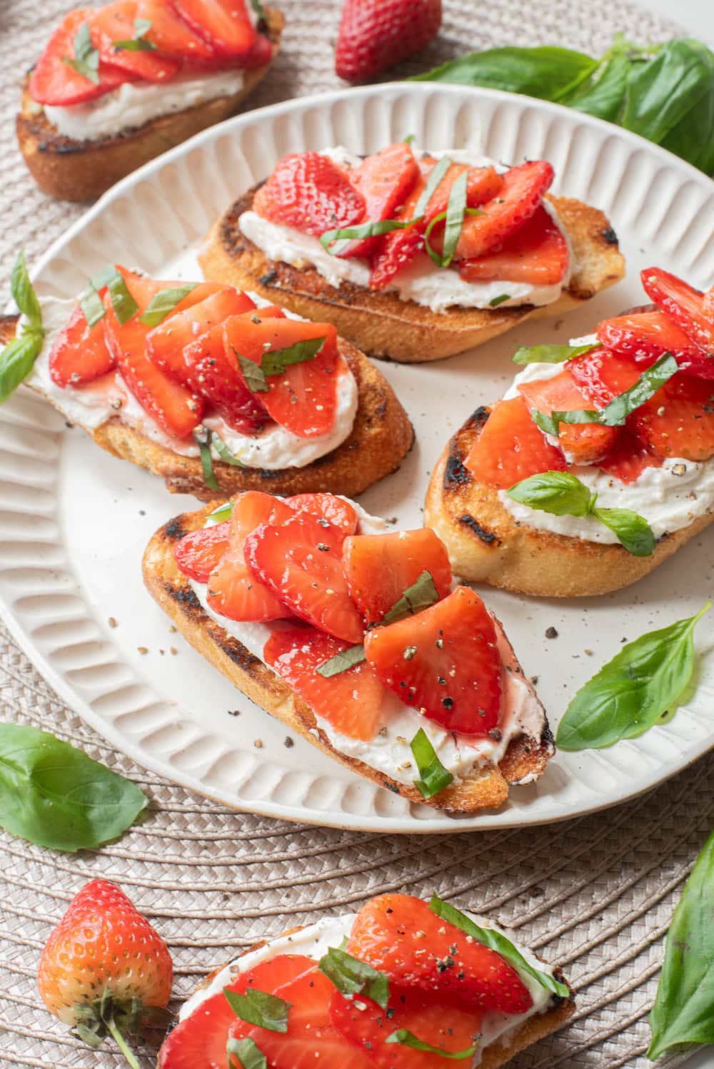 Plate of strawberry basil bruschetta topped with whipped lemon ricotta and fresh strawberries.