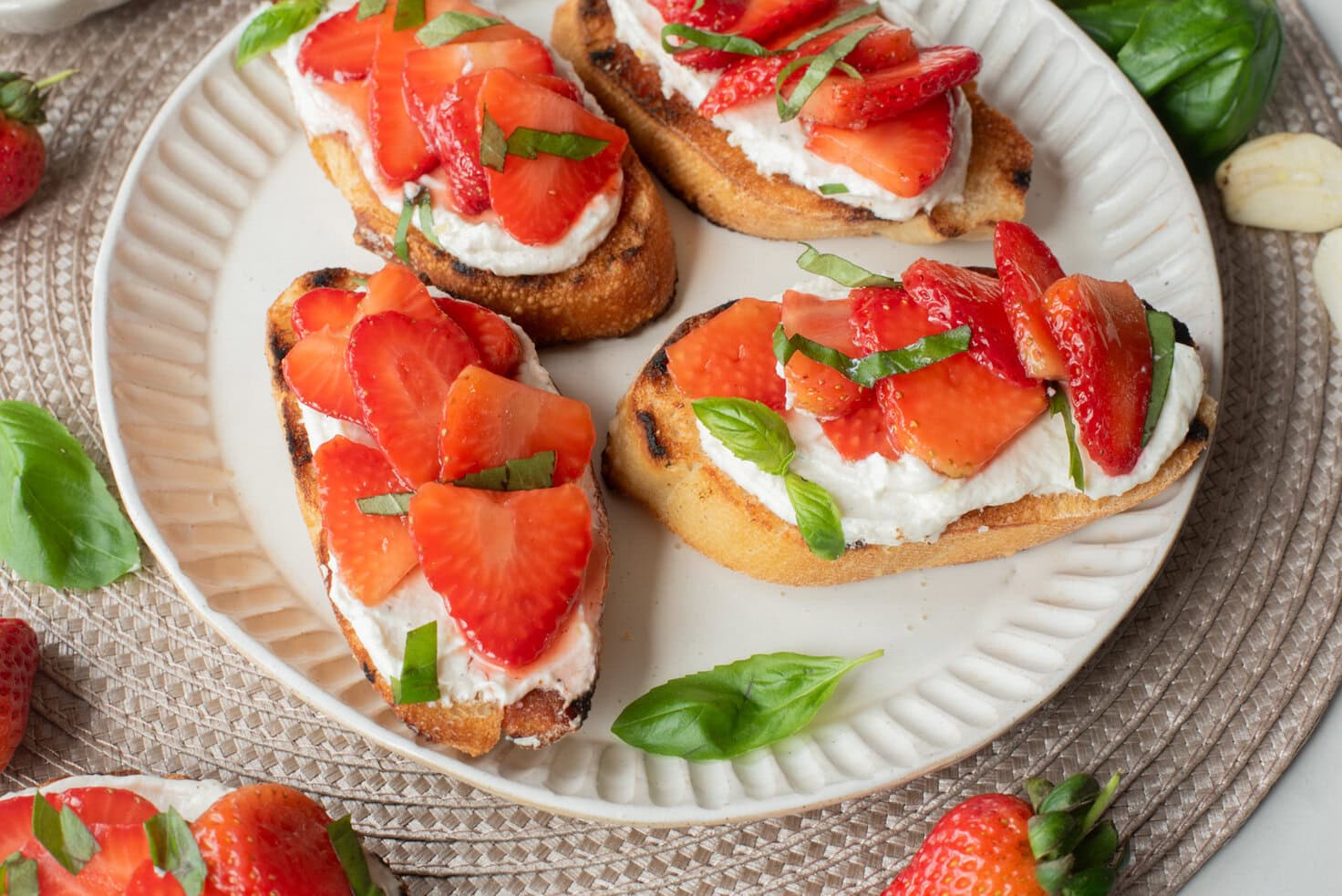 Strawberry basil bruschetta served on a plate with whipped ricotta and fresh basil leaves.