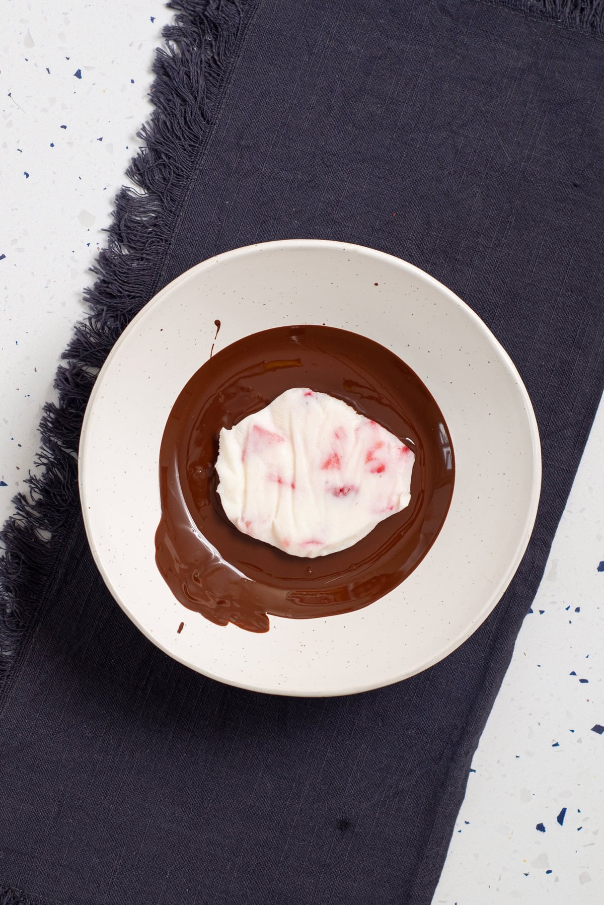Frozen strawberry cottage cheese cluster being coated in melted chocolate.