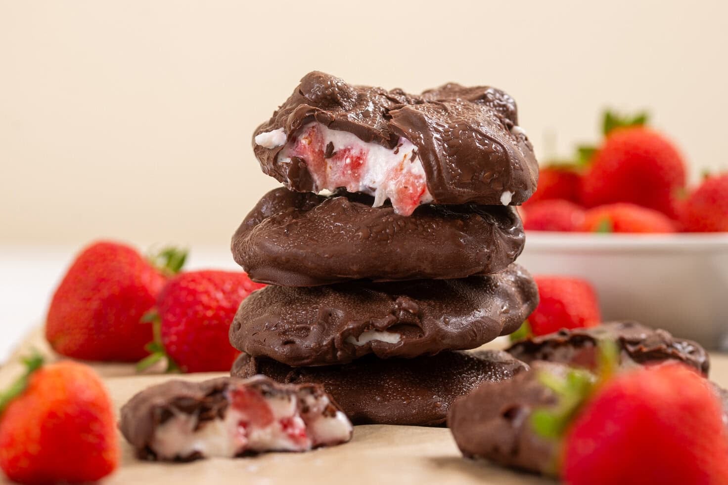 Strawberry cottage cheese chocolate clusters stacked on a board with fresh strawberries, featuring a creamy frozen strawberry filling inside a chocolate shell.