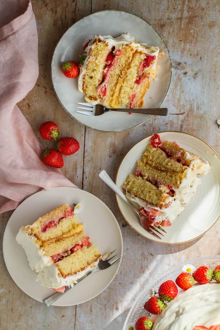 An overhead view of three slices of fresh strawberry cake with lemon curd placed on a white plate with fresh strawberries on the sides.