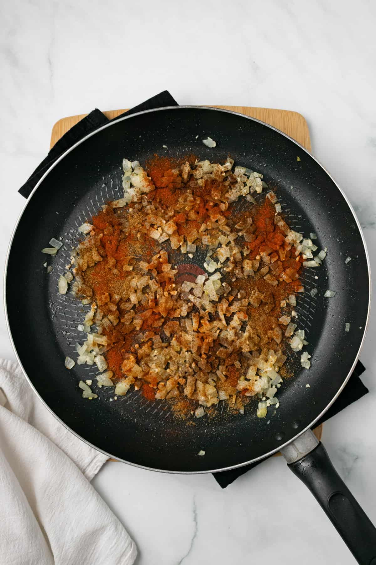 An overhead image of sauteing onions, garlic, and spices on a skillet.