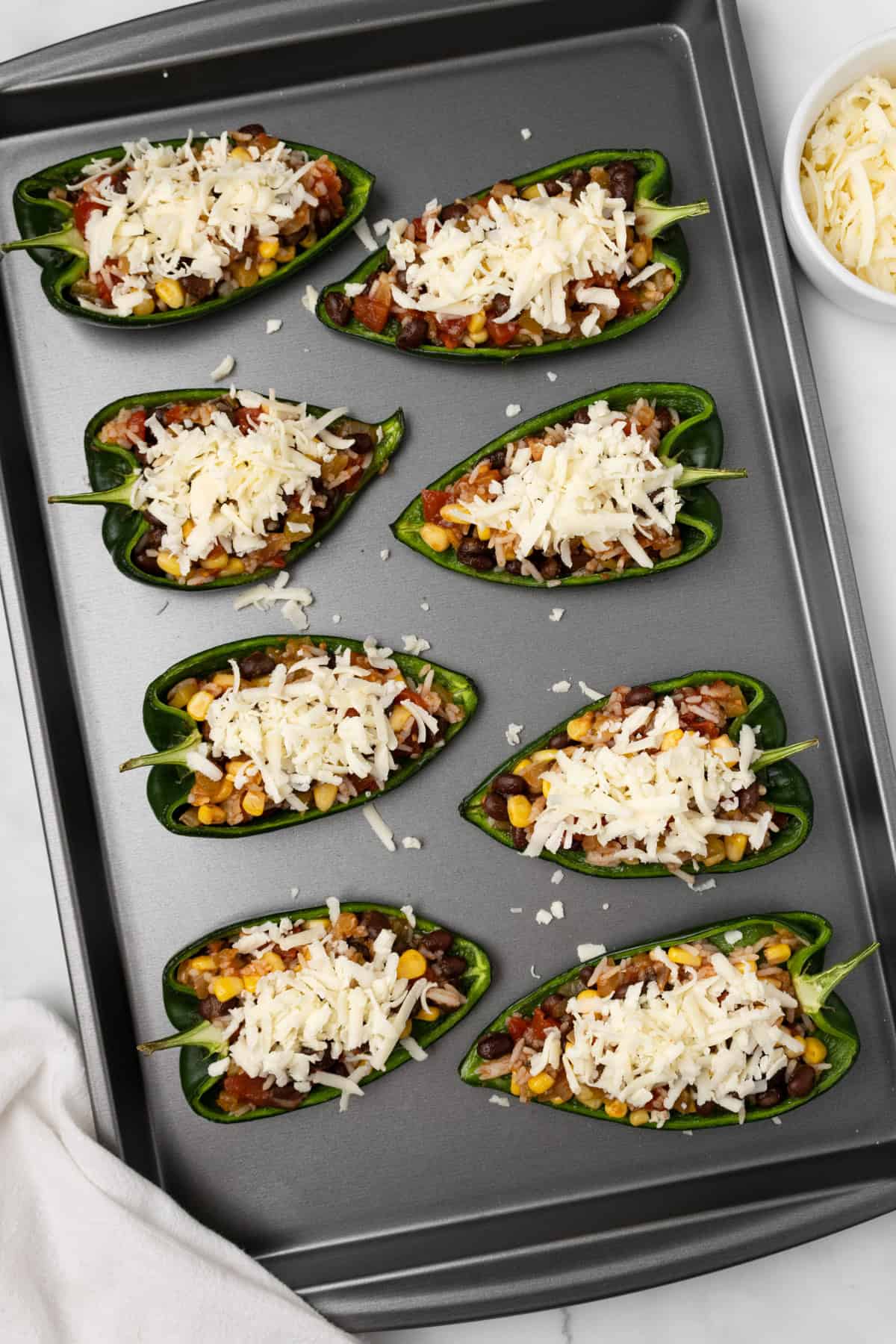 An overhead image of stuffed poblano peppers topped with cheese on a baking sheet.
