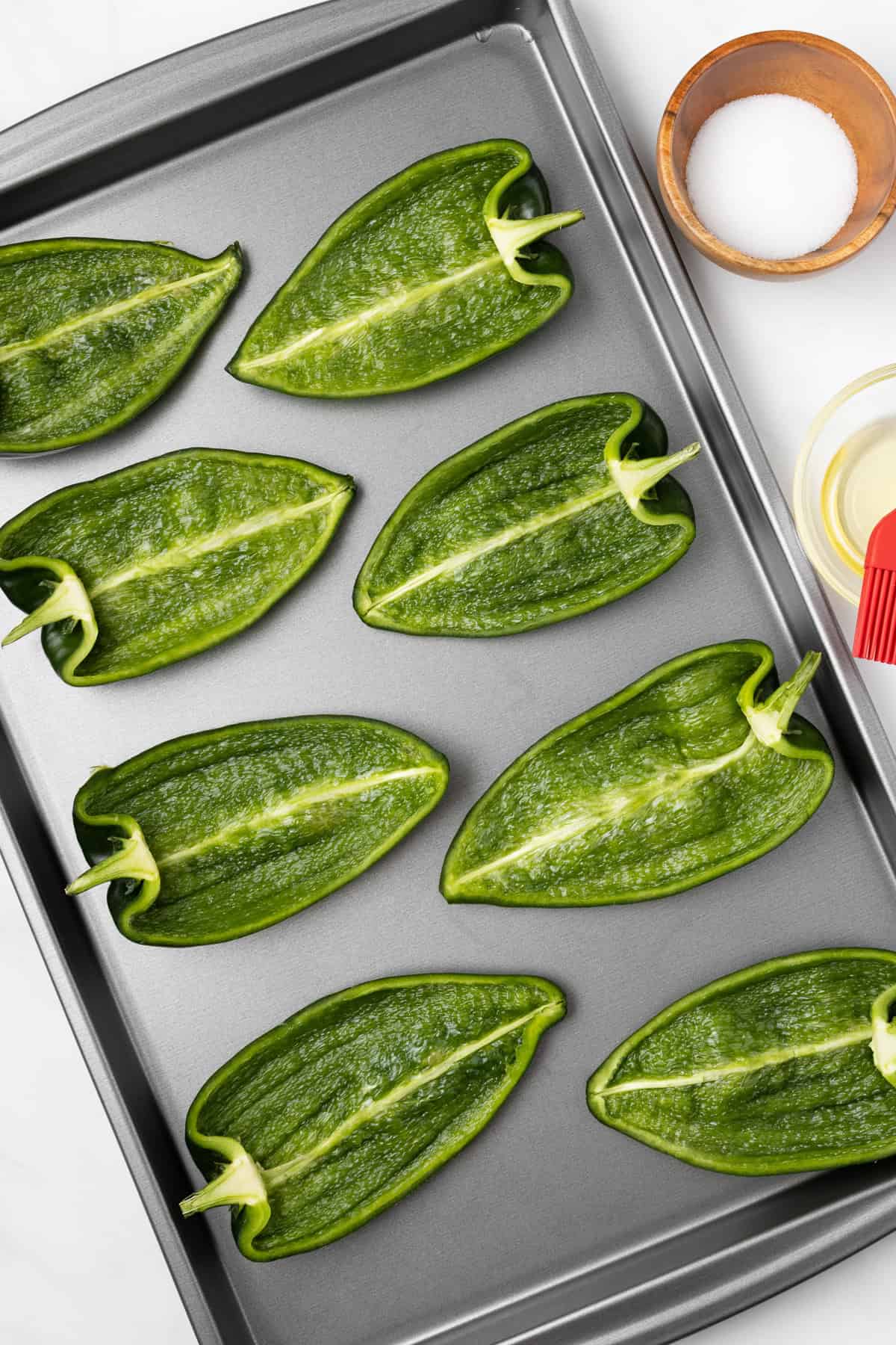 An overhead image of poblano pepper halves arranged on a baking sheet.