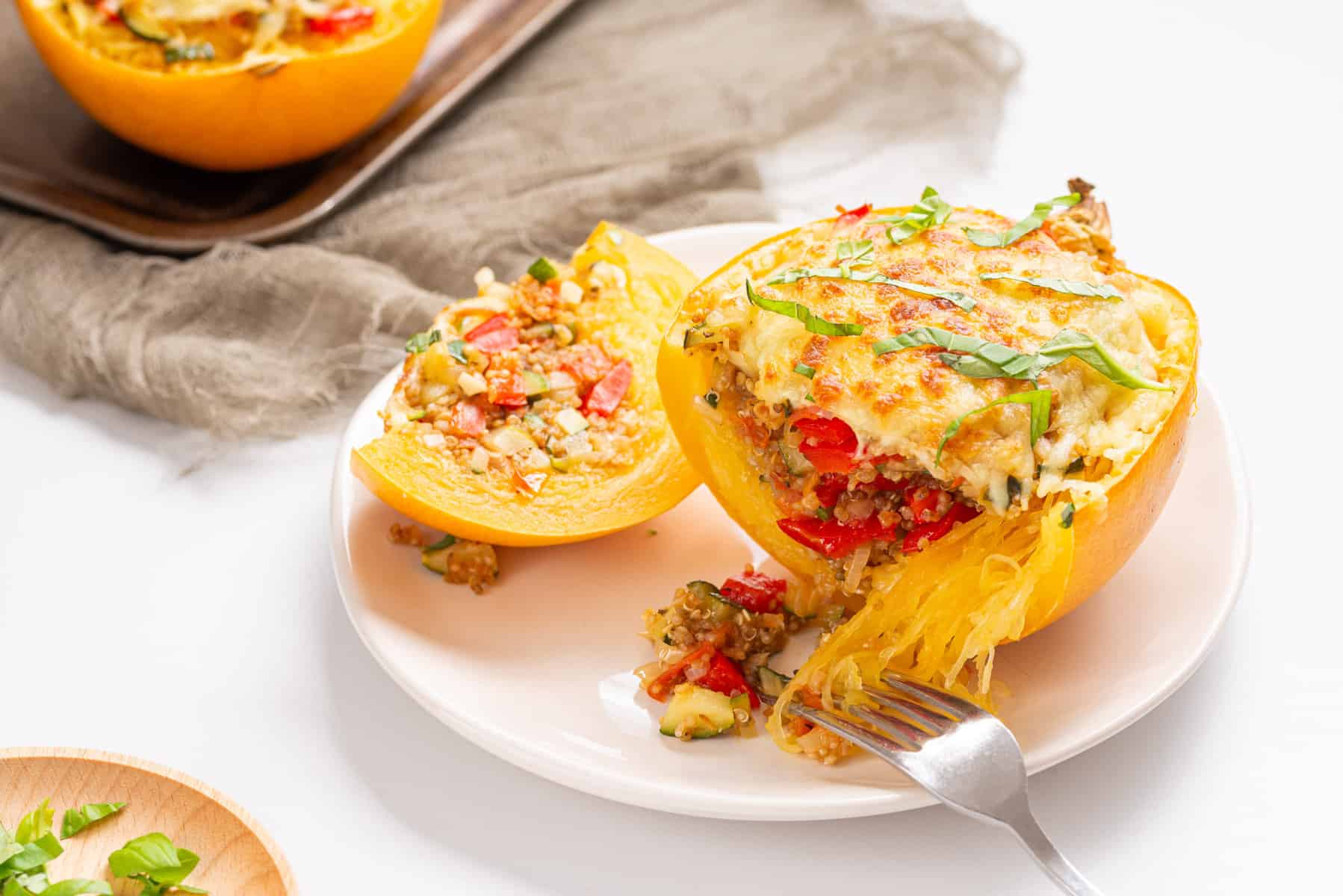 An image of two stuffed spaghetti squashes on a white plate with a fork  slicing a part of one of the squashes.