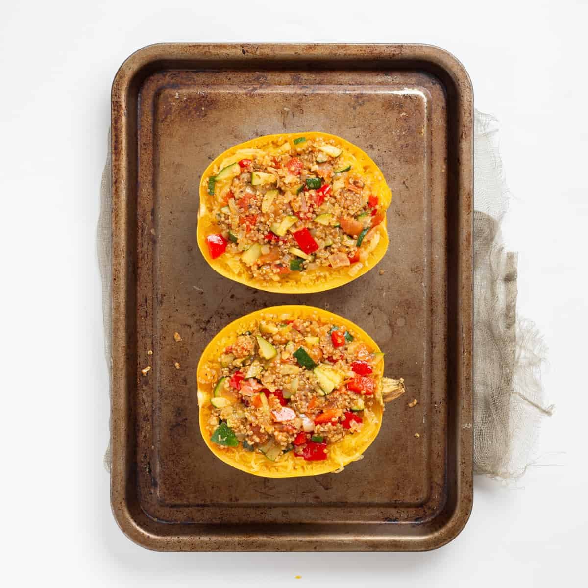 An overhead image of two spaghetti squash halves on a baking sheet, stuffed with sauteed vegetables.