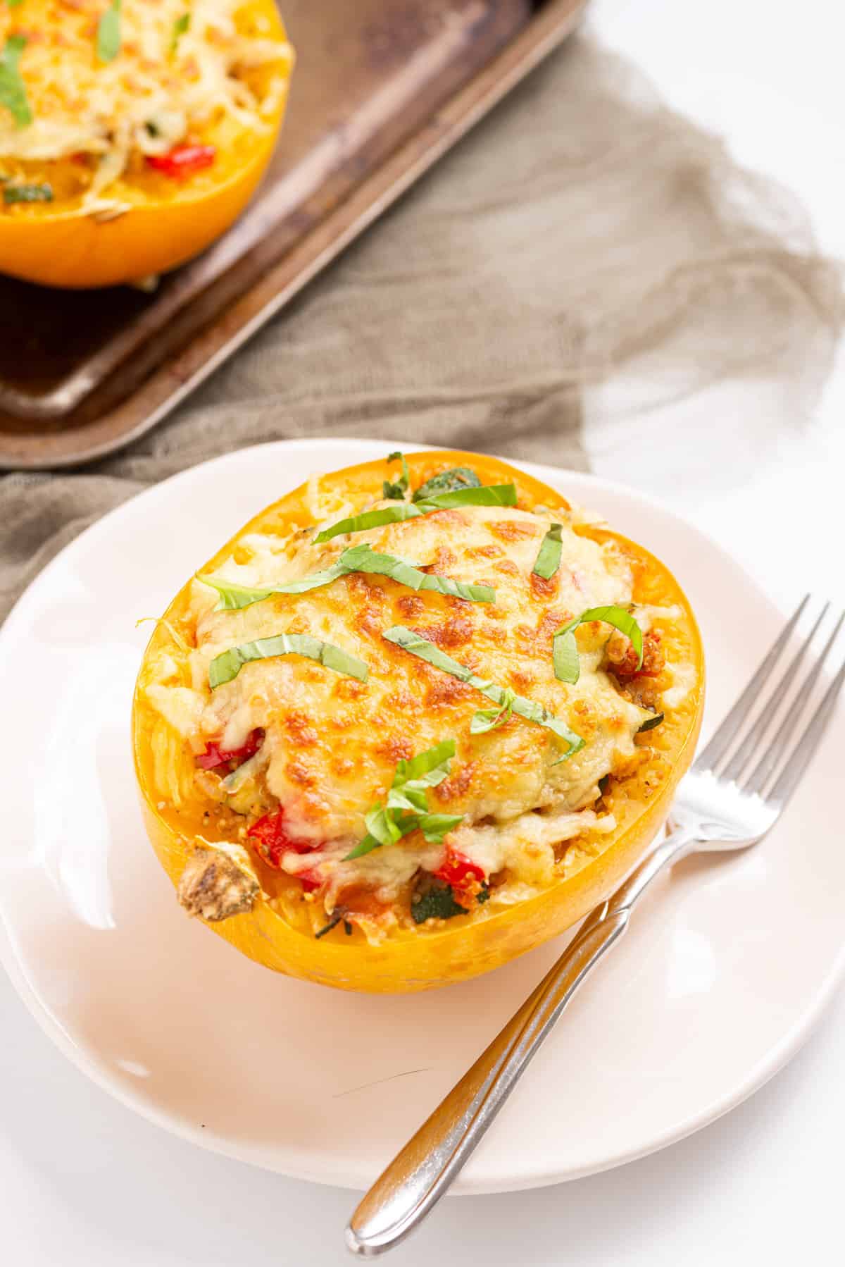 An image of stuffed spaghetti squash served on a white plate with a silver fork on the right side of it.