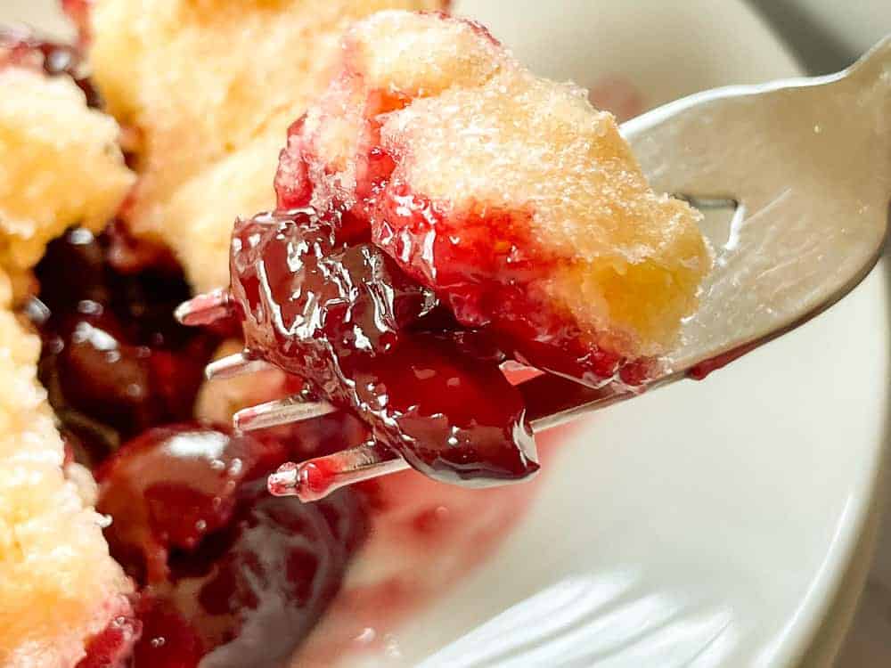 Close up showing a fork with a slice of cherry cobbler.