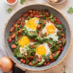 Sweet potato breakfast hash with eggs cooked in a skillet with spinach and bell peppers.