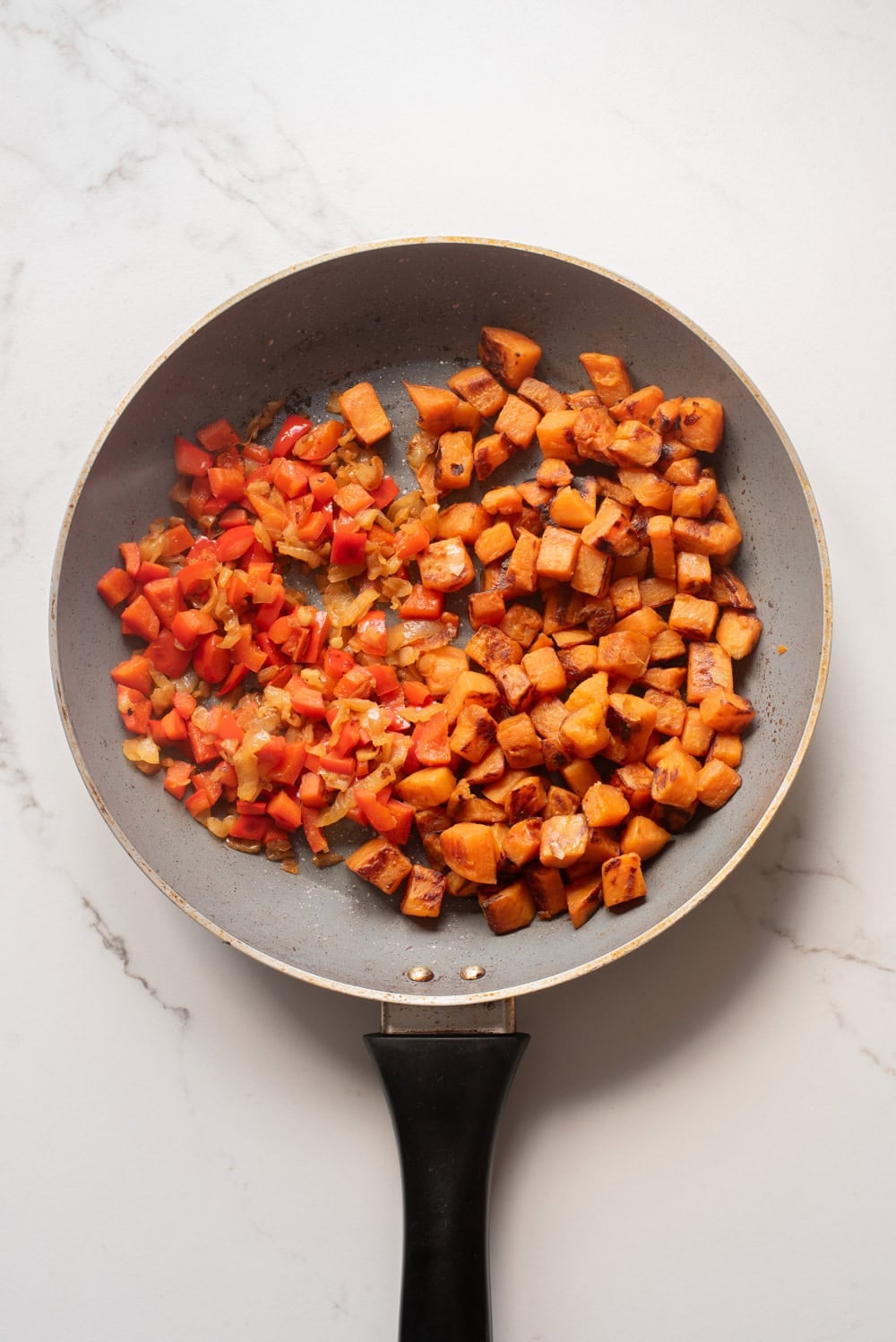 Sweet potatoes cooking with onion, bell pepper, garlic, and spices.