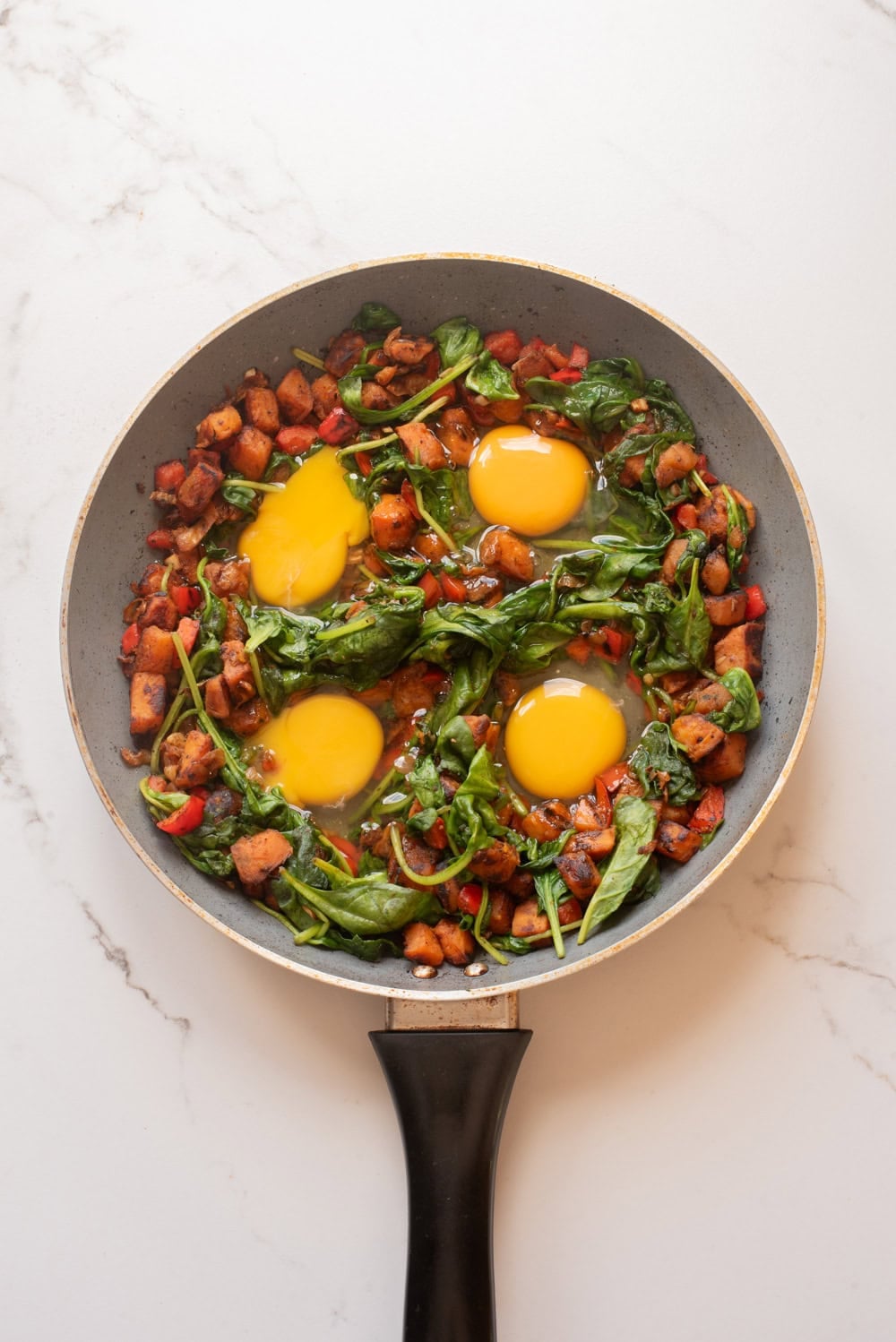 Eggs cracked into wells in the sweet potato hash.
