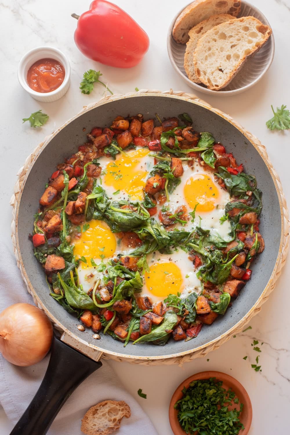 Finished sweet potato breakfast hash with cooked eggs and wilted spinach in a skillet.