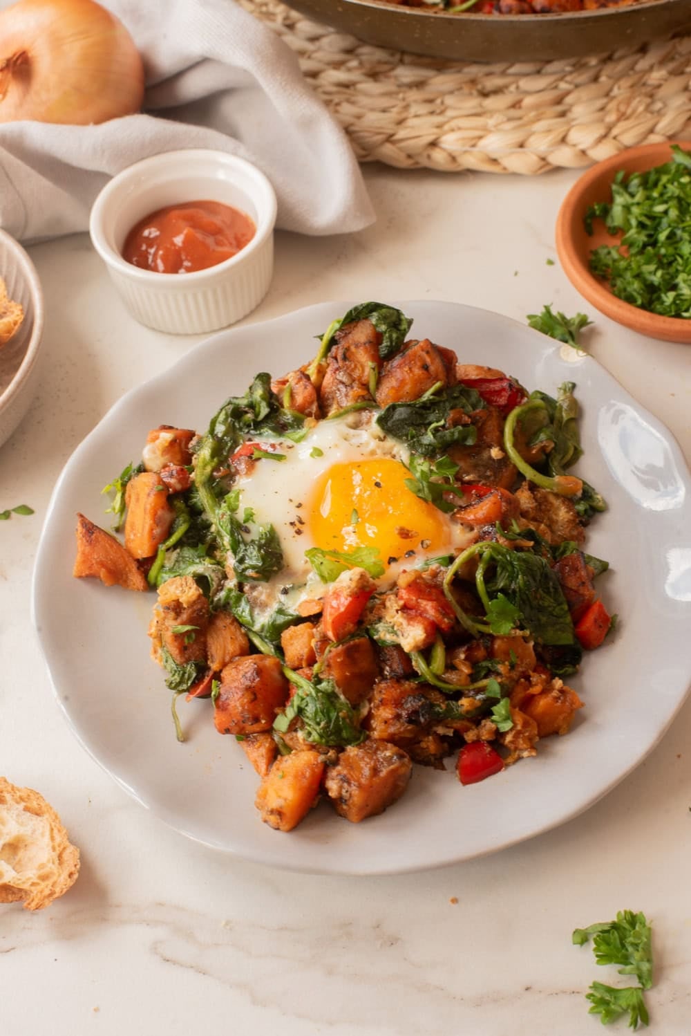 Plated sweet potato breakfast hash topped with a sunny-side-up egg and fresh spinach.