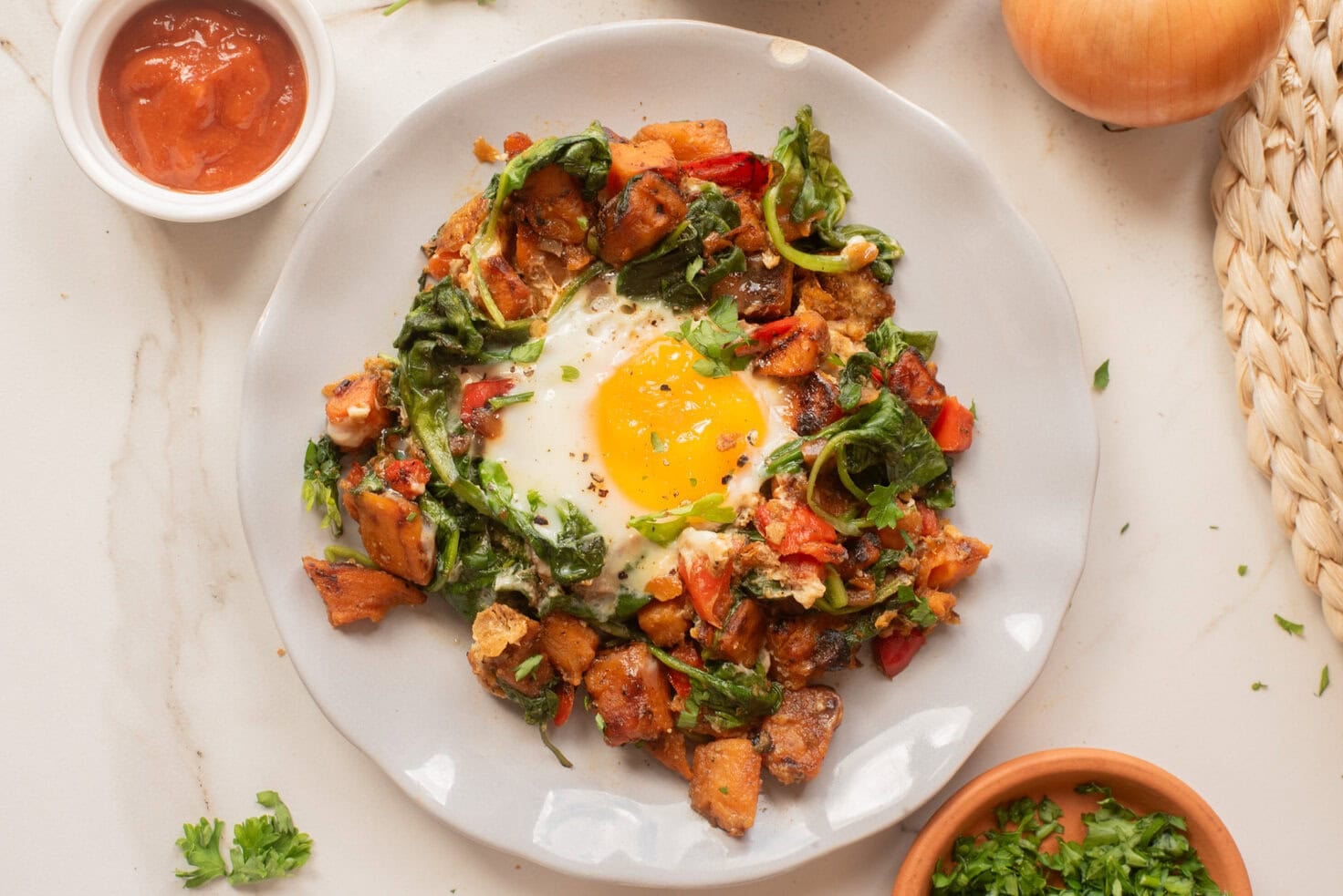 Plated sweet potato breakfast hash topped with a sunny-side-up egg and fresh spinach.
