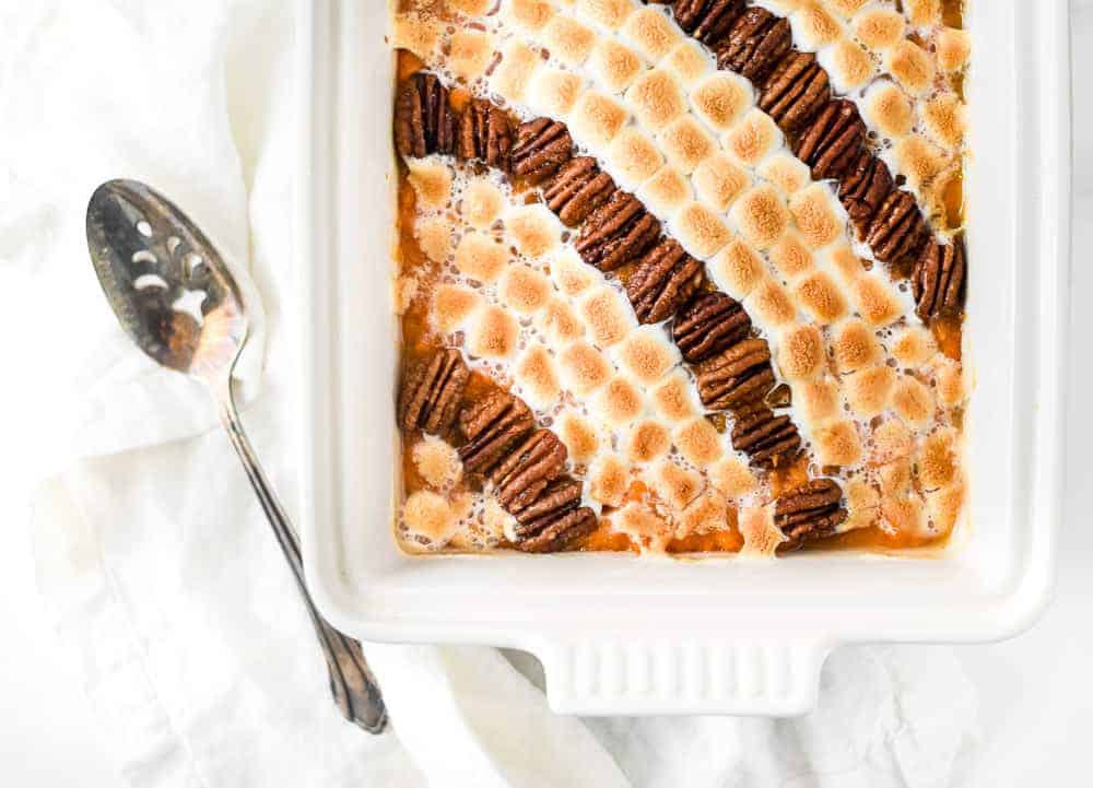 Overhead view of candied pecan marshmallow sweet potato arranged on a white casserole with spoon on the side.