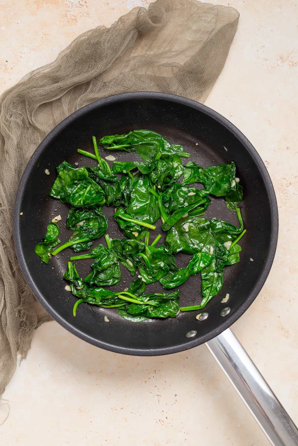 An overhead image of spinach and minced garlic in a skillet.