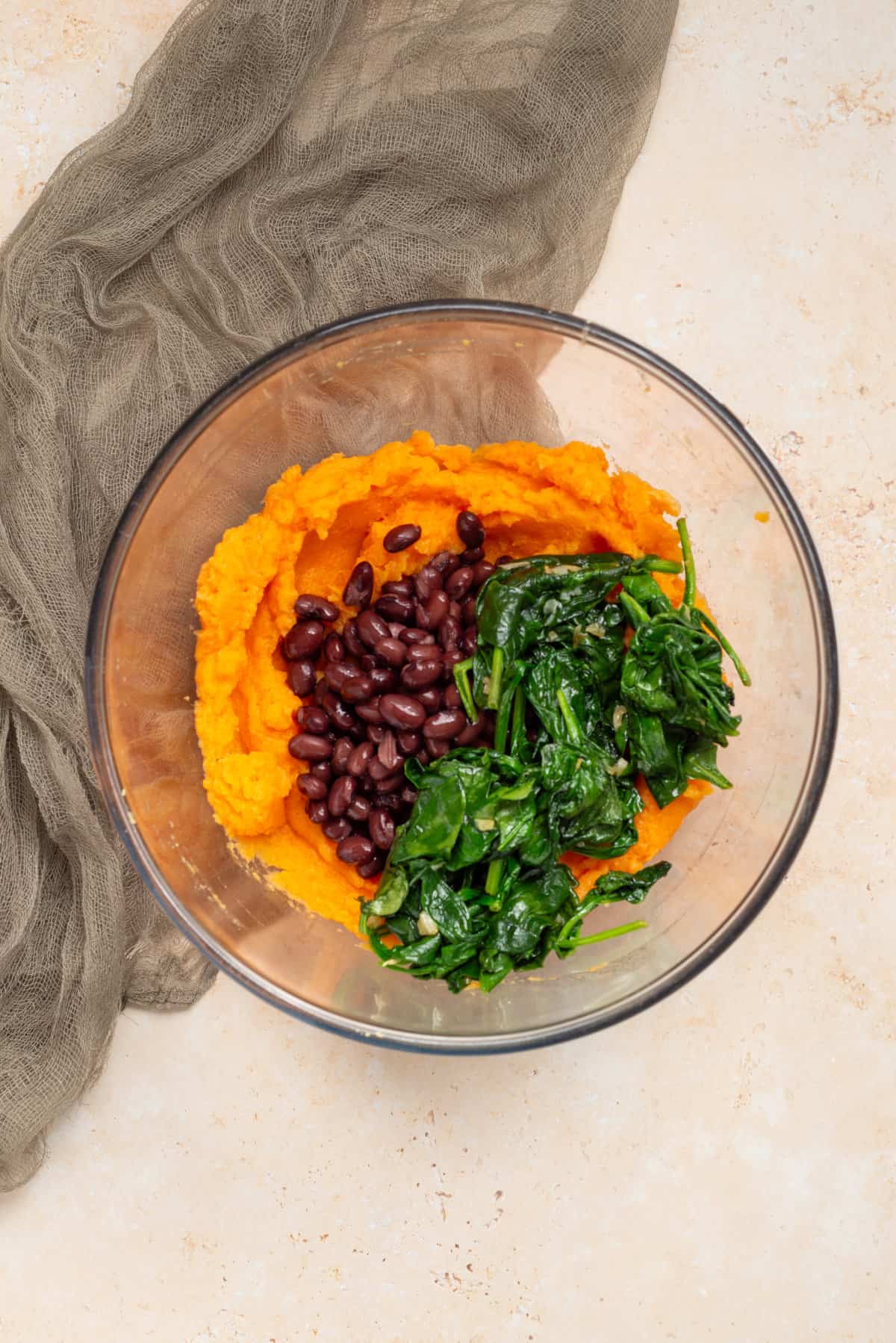 An image of sweet potato flesh, black beans, and spinach in a mixing bowl.