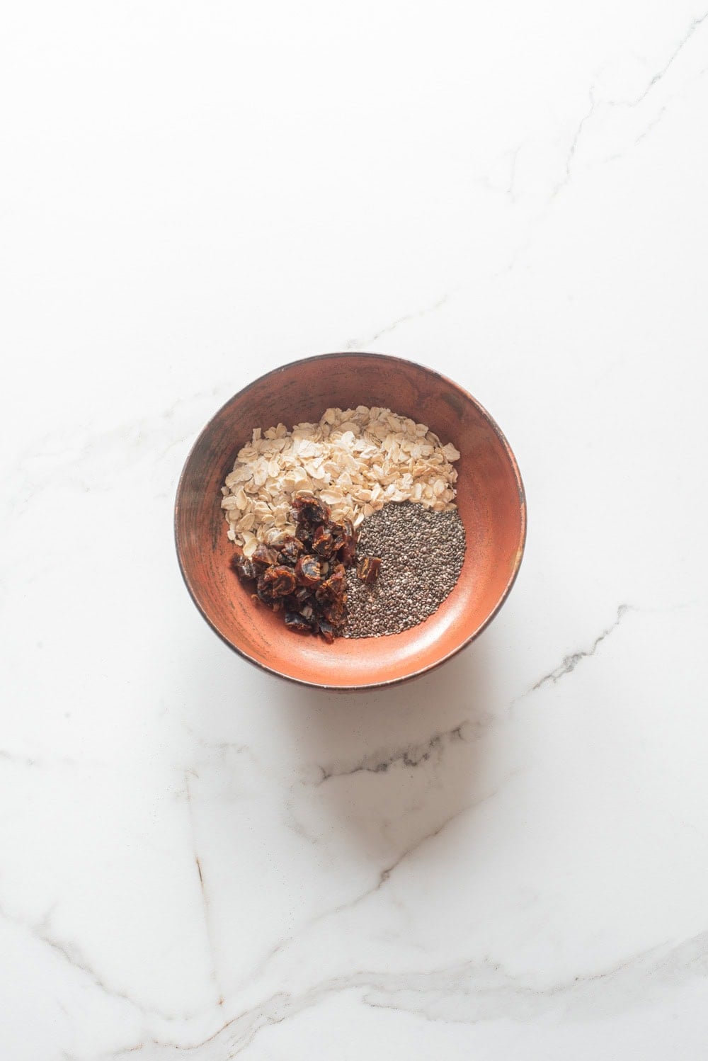 Rolled oats, medjool dates, and chia seeds in a bowl before mixing.
