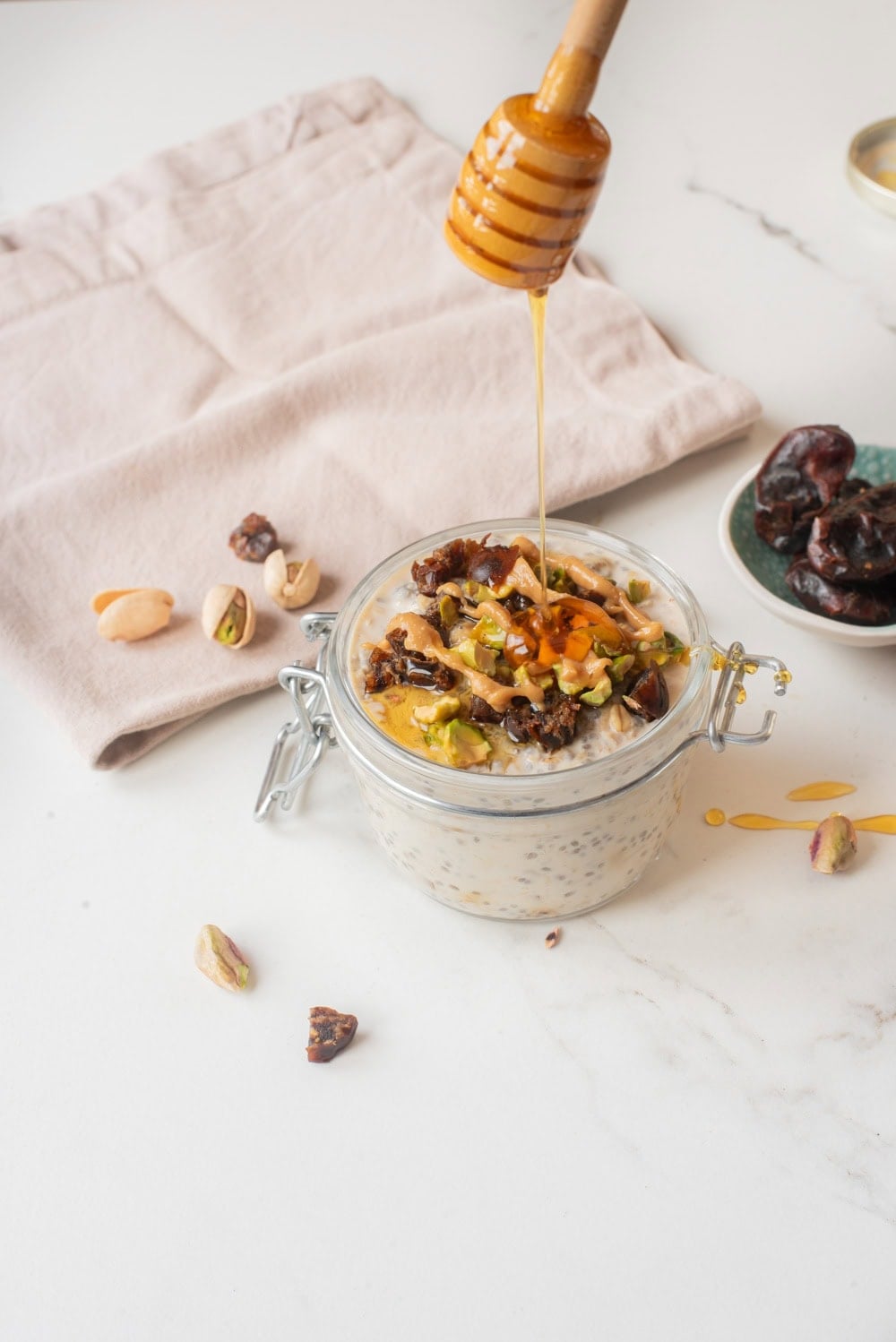 Honey being drizzled on top of tahini date overnight oats with toppings in jar.