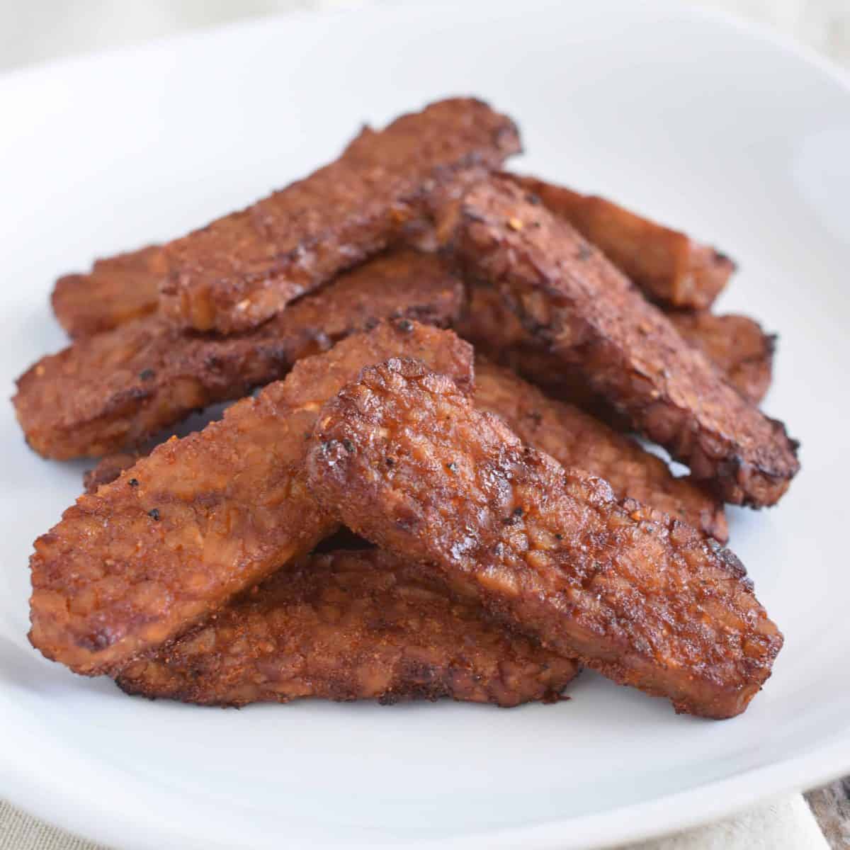 A straight view of air-fried tempeh bacon placed on a white plate.