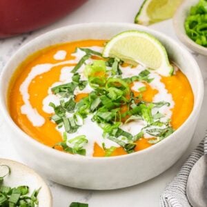 Bowl of Thai butternut squash soup topped with coconut milk, Thai basil, scallions, and lime,